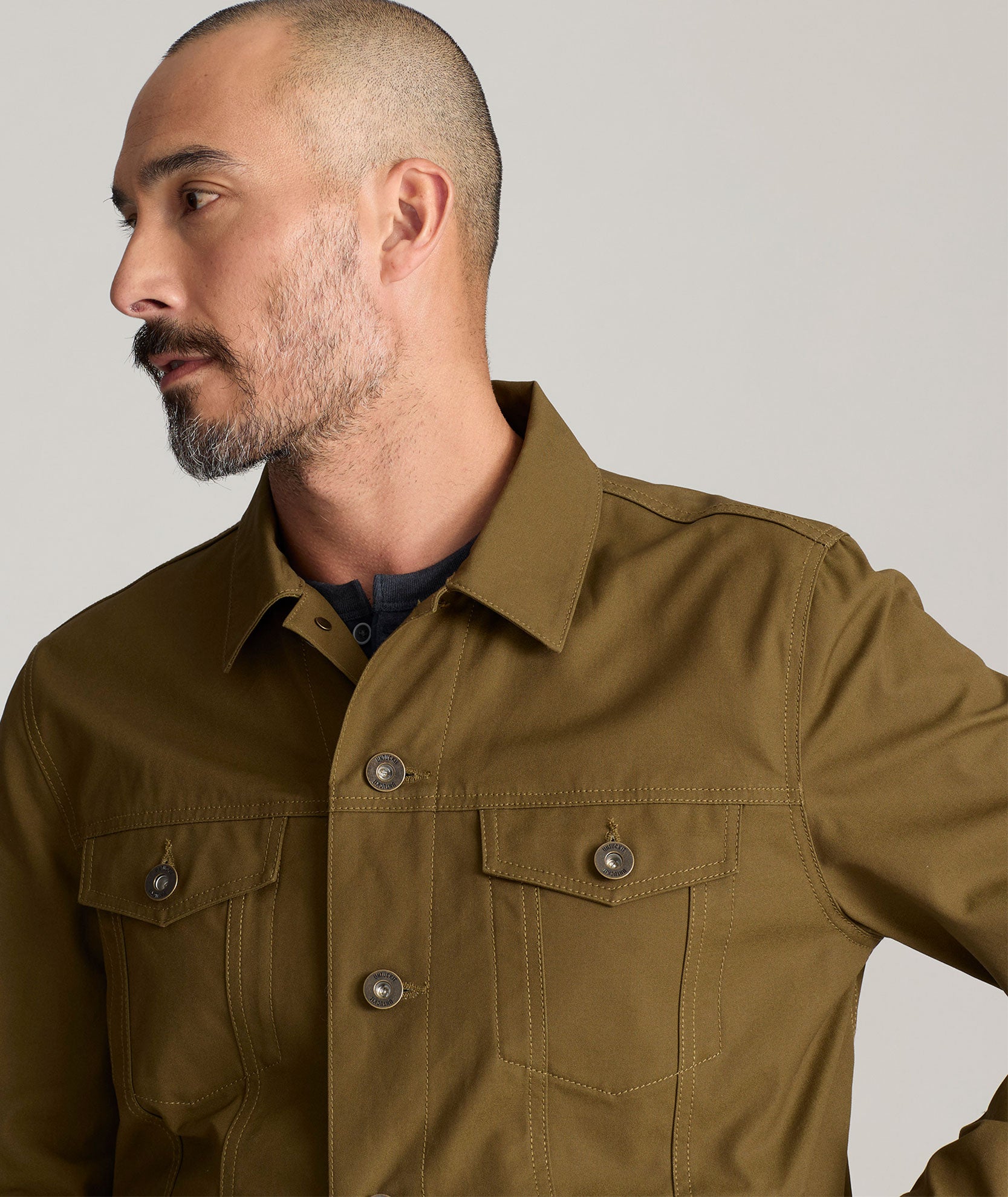 Model is wearing UNTUCKit Rizzo waxed trucker jacket in dark olive. 